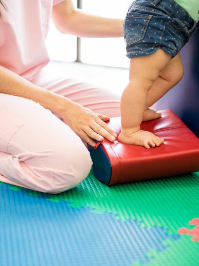 Closeup of a female therapist helping a baby with some balance exercises in an early stimulation school